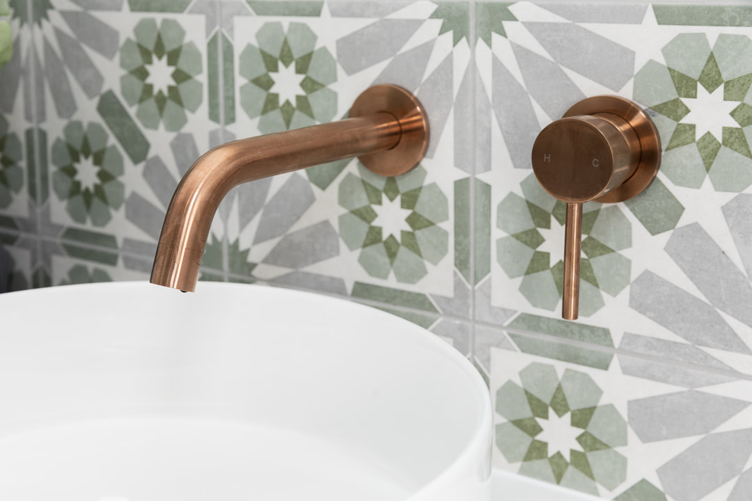 ABI Interiors brushed copper tapware against green and grey encaustic tile.