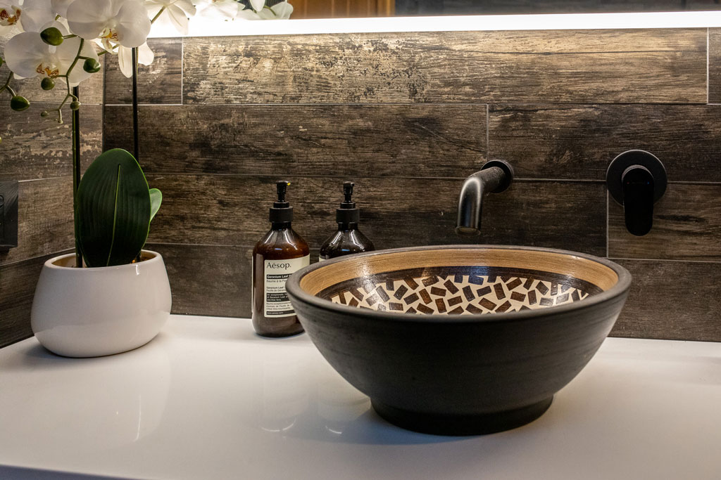ensuite bathroom in Alstonville NSW featuring patterned vanity vessel basin, stone benchtop, black tapware & dark timber plank tiles.