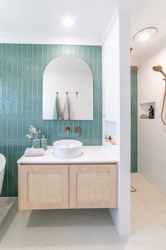 Coastal Bathroom in Lennox Head NSW by Northern Rivers Bathroom Renovations. Renovations features sage green subway wall tiles, arch mirror and light timber vanity with rattan cupboard doors.